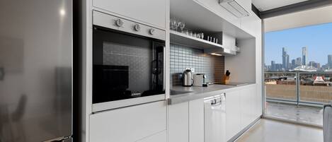 A modern kitchen with a stainless steel refrigerator, oven, and dishwasher. There is a window with a city view.