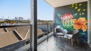 A balcony with a city view, two wicker chairs, and a mural of flowers. - Modern 1-bed, City Skyline Views & Close to Shops (Melbourne)