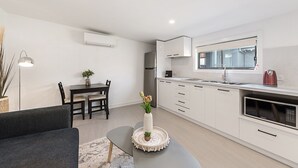 Una cocina moderna con armarios blancos, un comedor con mesa y sillas, y una sala de estar con un sofá y un jarrón de flores.