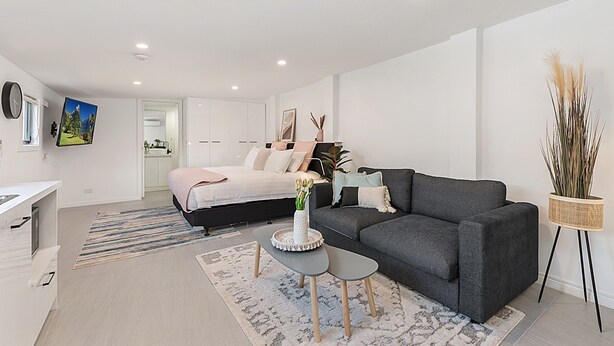 Un dormitorio moderno y luminoso con cama, mesita de noche y una pequeña zona de estar con sofá y mesa de centro.