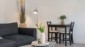 Una sala moderna con un sofá gris oscuro, una mesa redonda de centro con un jarrón blanco de tulipanes, una lámpara de pie alta y una zona de comedor con mesa y sillas de madera.
