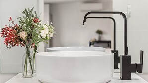 Un baño moderno con un lavamanos blanco, un grifo negro y un florero con flores en la encimera.