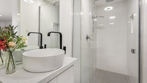 Un baño moderno con un lavabo blanco redondo, una cabina de ducha de vidrio y un espejo sobre el lavabo.