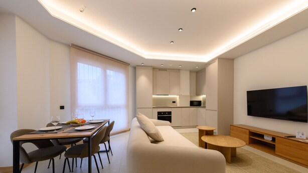 A modern living room with a sofa, dining table, and chairs. There is a kitchen area with cabinets and a TV mounted on the wall. - M Scr7b1 Amplio Piso Exterior de un Dormitorio e (Madrid)