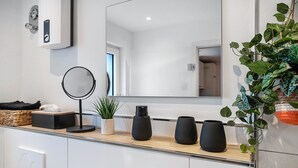 A modern bathroom with a large mirror, a round mirror, a potted plant, and black vases on the countertop.