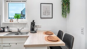 A modern kitchen with a window, a coffee maker, a sink, and a dining area with chairs and wooden boards.