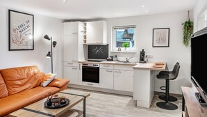 A modern kitchen with white cabinets, a built-in oven, a dining area with a wooden table, and a black chair.