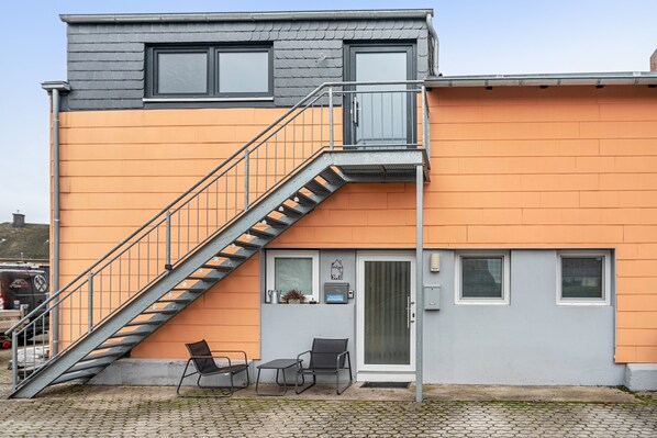 Ein zweistöckiges Gebäude mit grauem Dach, orangen Wänden und einer Metalltreppe, die zum oberen Stockwerk führt.