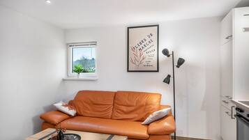 Una sala moderna con un sofá de cuero, una mesita, una lámpara de pie, una ventana con vistas y un cuadro enmarcado en la pared.