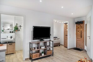 Ein modernes Wohnzimmer mit Flachbildfernseher, Holzmöbeln, einem Spiegel und einer kleinen Pflanze.