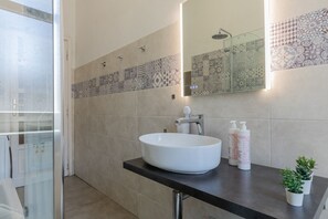 Un bagno moderno con un ampio lavabo bianco, cabina doccia in vetro e piastrelle decorate sulle pareti.
