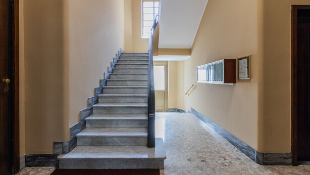 A staircase with marble steps and a handrail, leading to a landing with a window and a wall-mounted air conditioning unit. - Bramante Enchanting Home by Wonderful Italy (Turin)