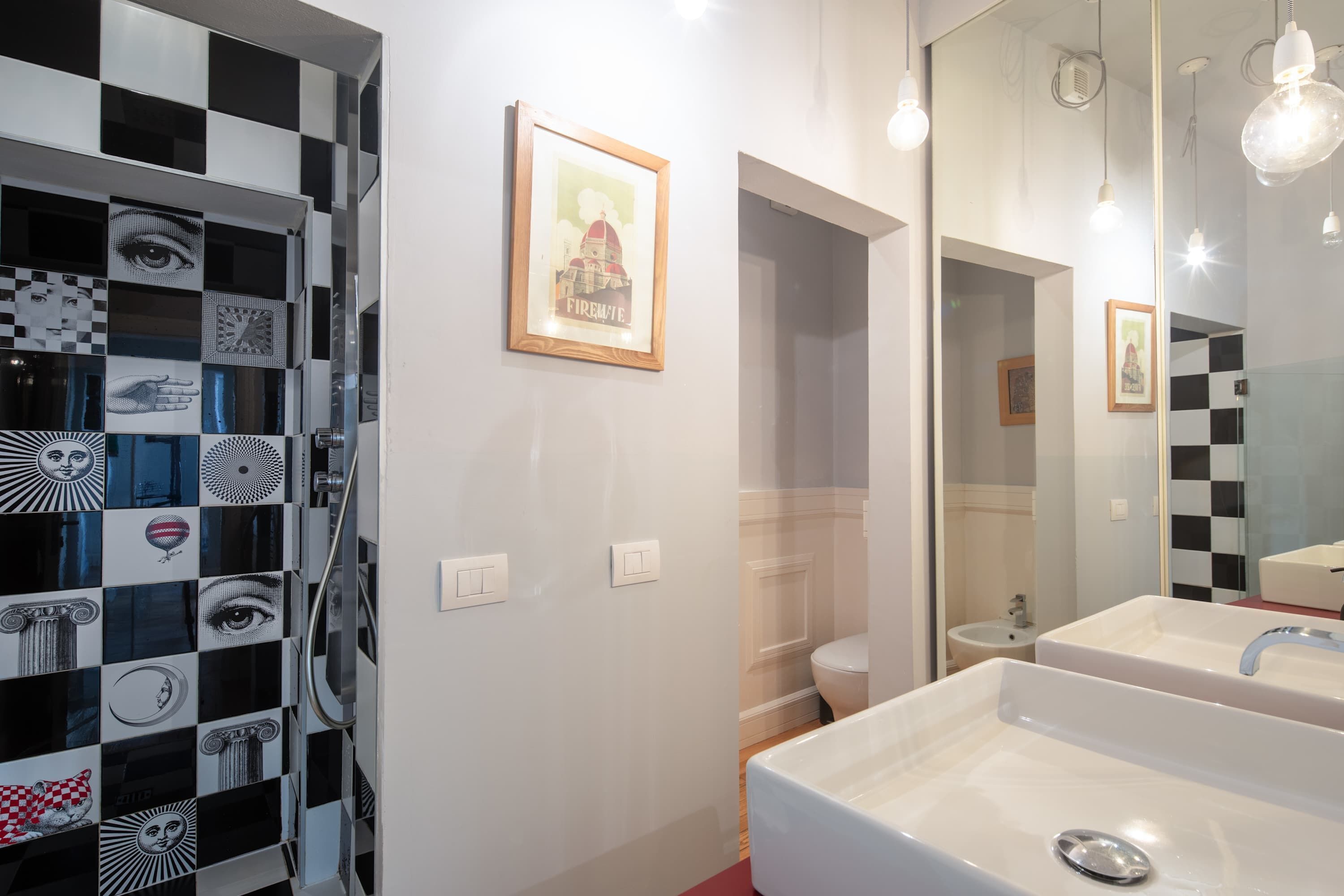 A bathroom with a checkered wall design, a framed picture, a sink, and a mirror.