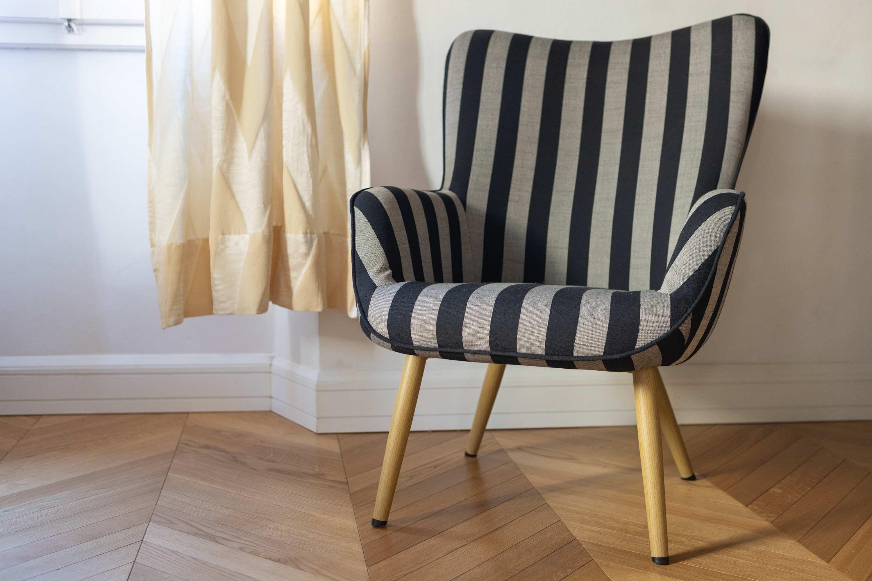 Un sillón a rayas con patas de madera en una habitación con suelo de madera y pared blanca.