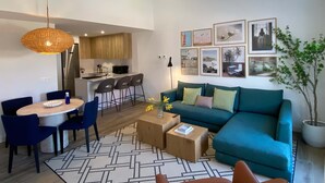 A modern living room with a teal sofa, a dining area with blue chairs, and a kitchen in the background. - w Modern 2BR With Terrace in Chueca (Madrid)
