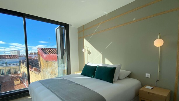 A modern bedroom with a large bed, a nightstand, a floor lamp, and a view of the city through a large window. - w Modern 2BR With Terrace in Chueca (Madrid)