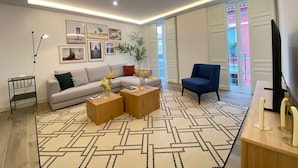 Una sala de estar moderna con un sofá, una mesa de centro y un televisor. Hay cuadros enmarcados en la pared y una planta sobre la mesa de centro.