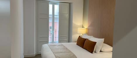 Habitación de hotel con cama, mesita de noche, lámpara y vistas al balcón exterior.
