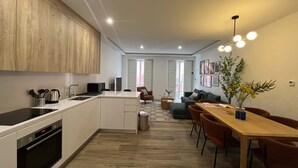 A modern kitchen with a central island, a dining area with a wooden table and chairs, and a living area with a sofa and a coffee table. - w Impressive 3BR w Sunny Terrace in Chueca (Madrid)