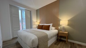 A bedroom with a large bed, a bedside table with a lamp, a window with curtains, and a wooden floor. - w Impressive 3BR w Sunny Terrace in Chueca (Madrid)