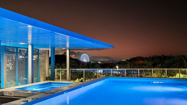 Un área de piscina moderna al aire libre con una vista despejada de una noria en el fondo.