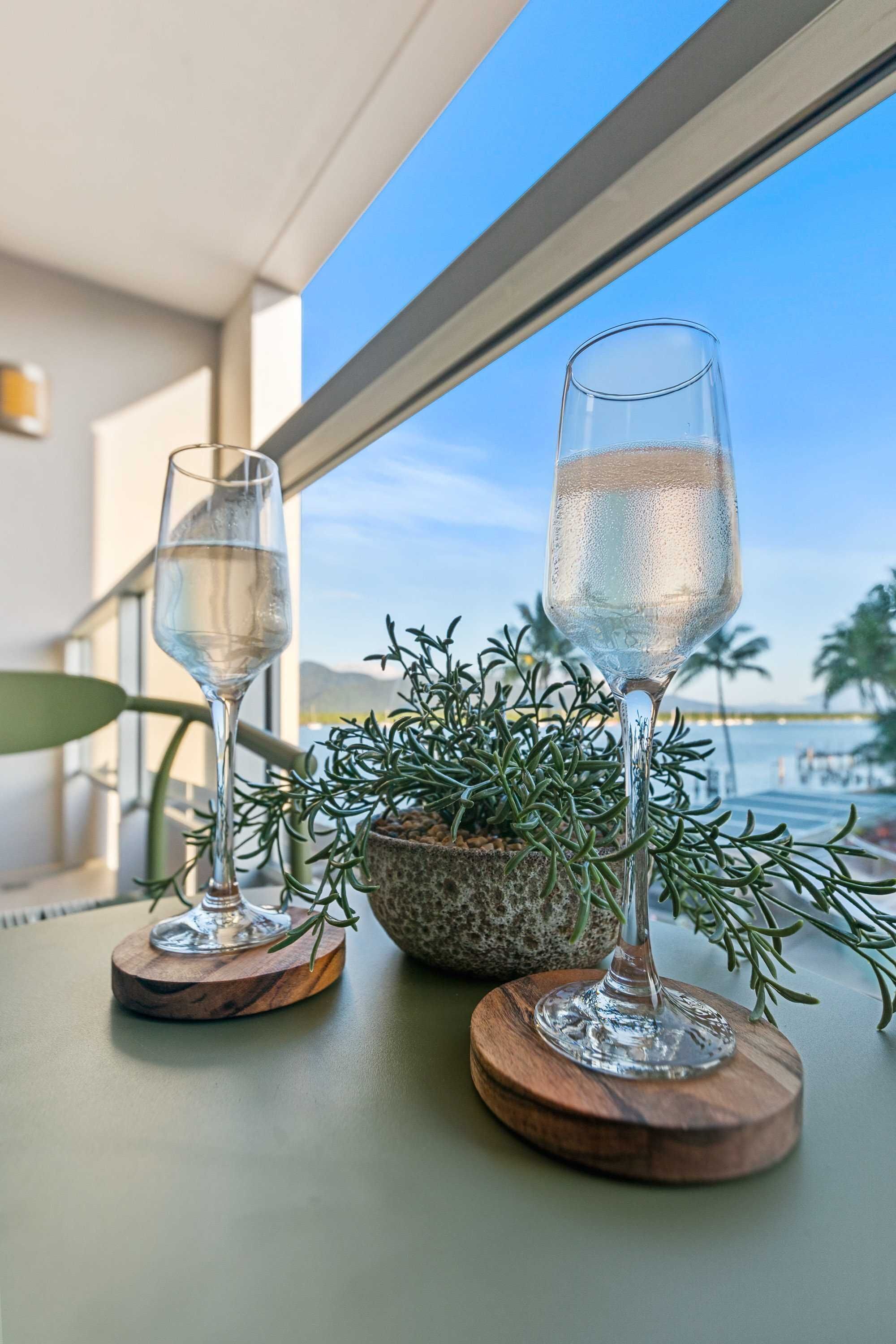 Dos vasos de agua sobre posavasos de madera en un balcón con vista al mar y a las montañas.