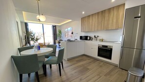 Una cocina moderna con armarios blancos, un refrigerador de acero inoxidable y una zona de comedor con una mesa redonda y sillas.