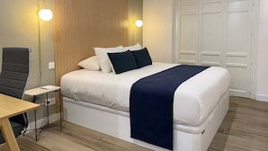 Una habitación de hotel con cama, mesita de noche, lámpara, silla y armario.