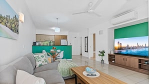 A modern living room with a grey sofa, a wooden coffee table, and a flat-screen TV. - Urban Tropics Modern Resort Apartment (Cairns)