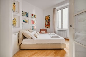 A bedroom with a bed, pillows, a chair, and artwork on the wall.