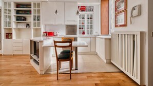 Una cocina moderna con armarios blancos, un comedor con una silla de madera y un hervidor rojo.