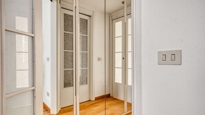 Un pasillo con suelo de madera, paredes blancas y una puerta con paneles de vidrio esmerilado.