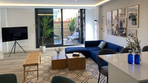 Un soggiorno moderno con TV a schermo piatto, un divano blu, un tavolo da pranzo e un'ampia finestra che si affaccia su un cortile.