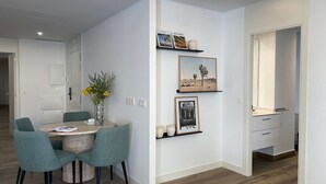 Un soggiorno moderno con zona pranzo, che include un tavolo rotondo con sedie, un vaso con fiori e mensole a parete con quadri.
