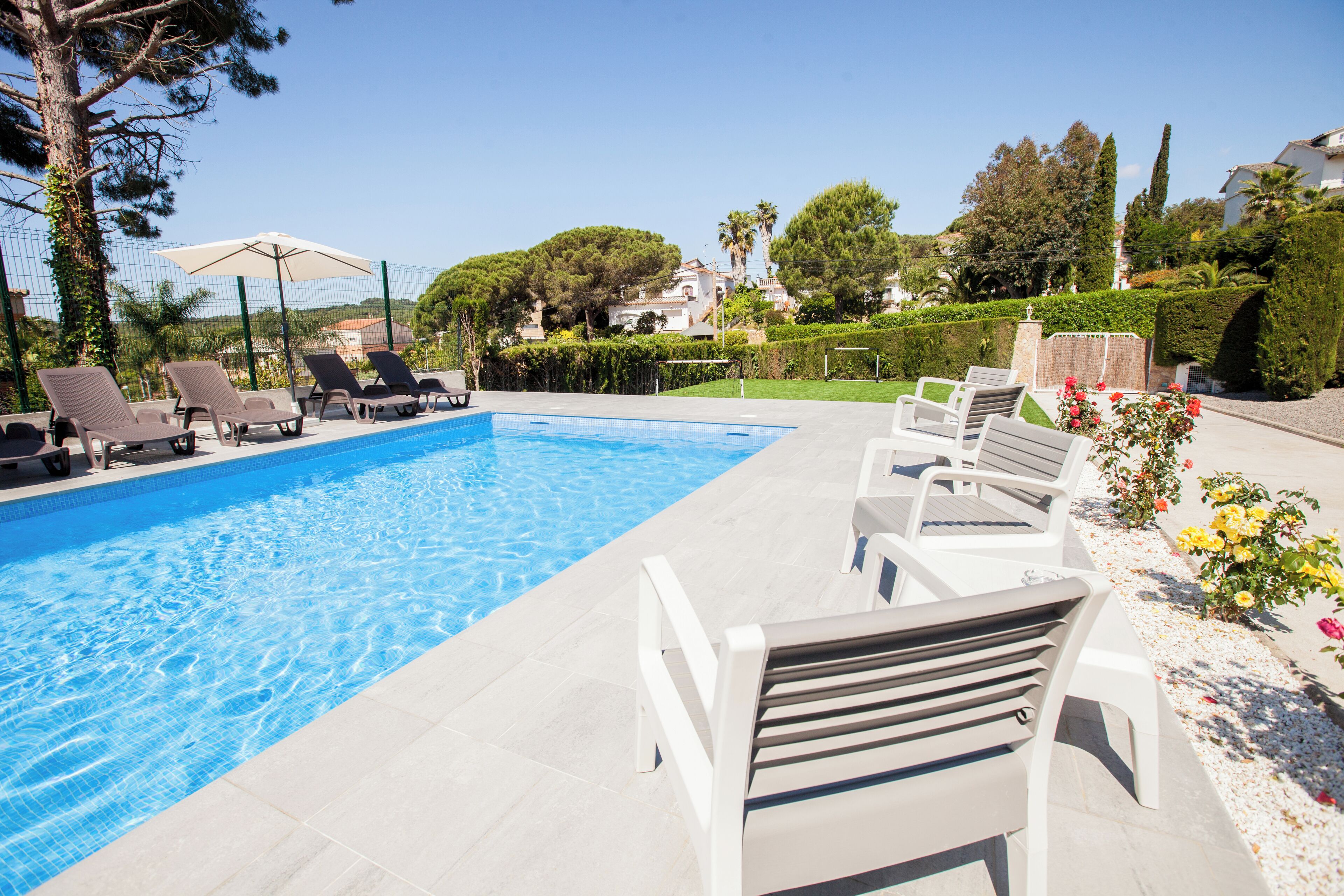Una piscina con sillas de descanso y un banco, rodeada de vegetación y edificios.