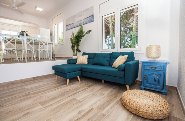 A modern living room with a teal sectional sofa, a woven ottoman, and a blue sideboard.