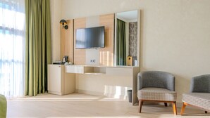 A modern hotel room with a flat-screen TV, a small kitchenette, and two grey armchairs. - Ayçiçeği Comfort Hotel (Edirne)