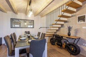 Un coin repas avec une longue table dressée pour six personnes, un miroir au mur et une table d’appoint originale sur le thème de la moto.