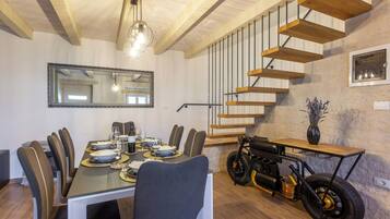 A dining area with a long table set for six, a modern chandelier, and a unique motorcycle-themed side table.