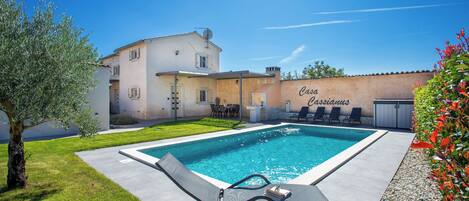 A swimming pool with lounge chairs, a table, and a building with a sign reading "Casa Cassandras."