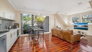 A modern kitchen with a dining area, a sofa, and a TV. - Stunning 2-bed Unit With BBQ Patio Near Dining (Melbourne)