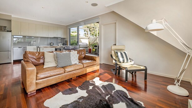 A modern living room with a leather sofa, a patterned rug, and a dining area with a kitchen in the background. - Stunning 2-bed Unit With BBQ Patio Near Dining (Melbourne)
