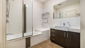 A modern bathroom with a glass-enclosed shower, a vanity with a mirror, and a dark wooden cabinet. - Stunning 2-bed Unit With BBQ Patio Near Dining (Melbourne)