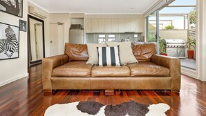 A spacious living room with a leather sofa, a large window, and a view of the outdoor patio area. - Stunning 2-bed Unit With BBQ Patio Near Dining (Melbourne)