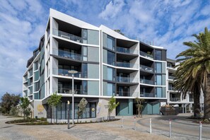 A modern multi-story hotel with balconies, a landscaped courtyard, and a palm tree. - Fremantle 1-bed Close to Beach & Shops (Perth)