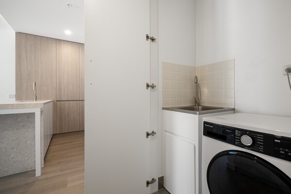 A compact laundry room with a washing machine, a sink, and a cabinet. - Fremantle 1-bed Close to Beach & Shops (Perth)