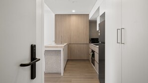 A modern kitchen with a wooden accent wall, a built-in oven, and a black microwave. - Fremantle 1-bed Close to Beach & Shops (Perth)