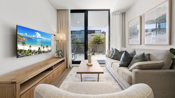A modern living room with a large TV, a sofa, a coffee table, and a view of the outdoors. - Fremantle 1-bed Close to Beach & Shops (Perth)