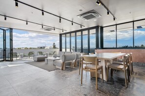 A modern rooftop lounge with a large table and chairs, a sofa, and a view of the city skyline. - Fremantle 1-bed Close to Beach & Shops (Perth)