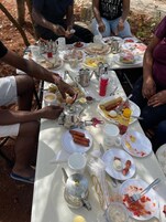 Un grupo de personas sentadas alrededor de una mesa con diferentes alimentos y bebidas, como salchichas, huevos y café.